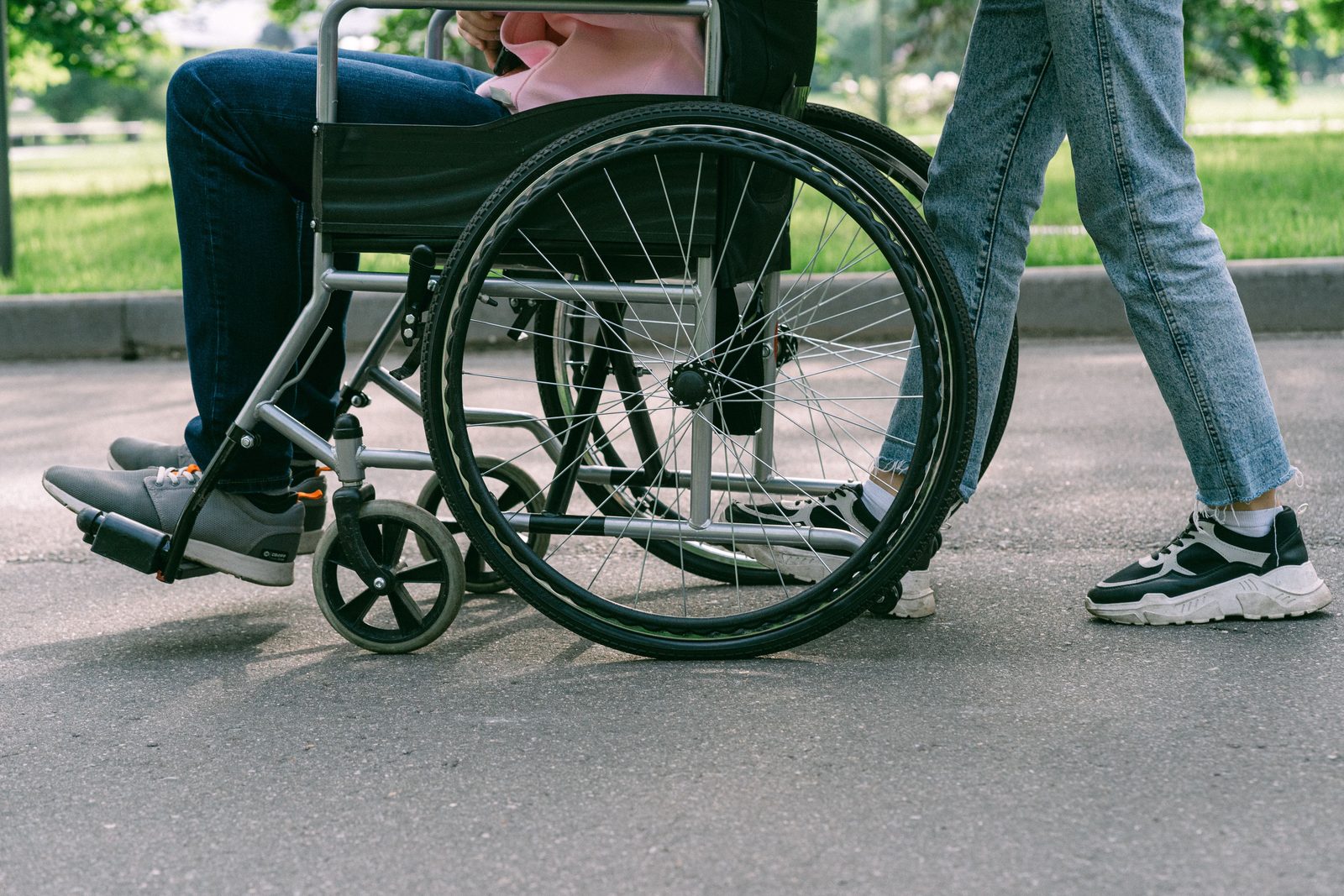 A support worker pushing someone in a wheelchair through a park